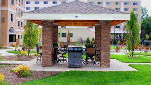 Un espace extérieur abrité, doté de piliers en briques, d’un barbecue et de mobilier d’extérieur.