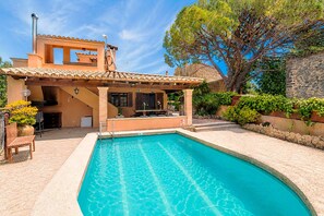 Une piscine bordée de pierres, une terrasse en bois et un espace patio couvert.
