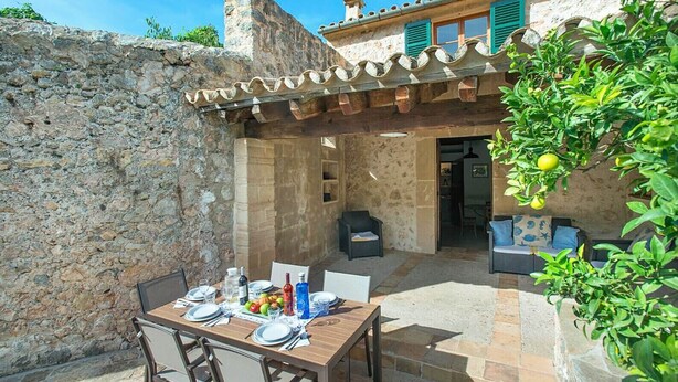 An outdoor dining area with a stone wall, a wooden table set for two, and a cozy seating area with a sofa and chairs.