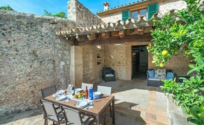 An outdoor dining area with a stone wall, a wooden table set for two, and a cozy seating area with a sofa and chairs. - 3 bedroom villa, with private pool and BBQ, Pollensa (Pollensa)