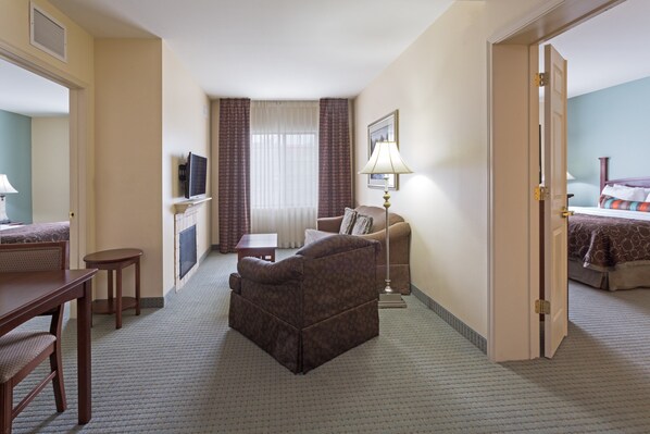 A hotel room with a sofa, a small table, a lamp, a TV, and a bed with a patterned bedspread.