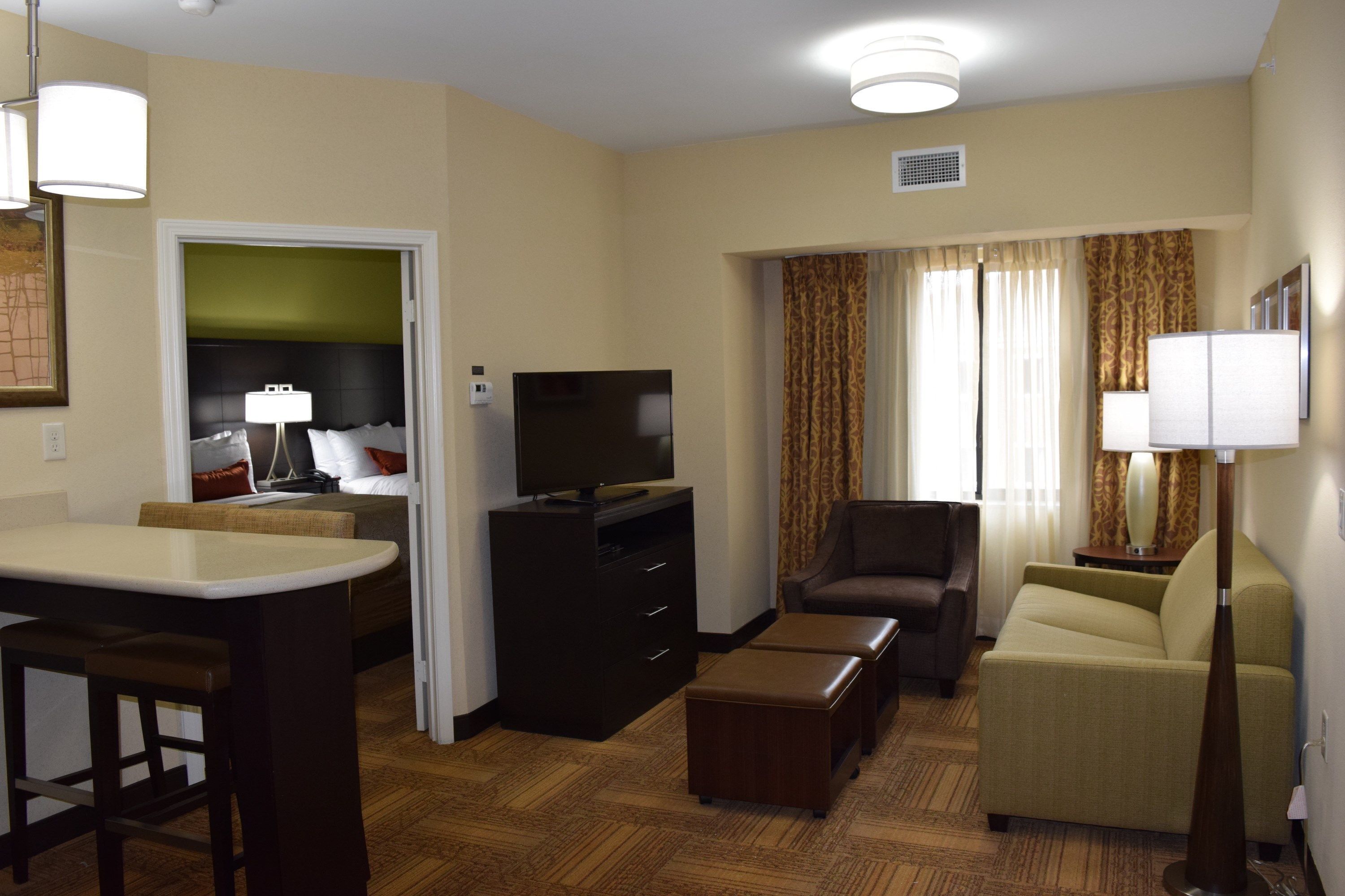 A hotel room with a dining area, a sofa, a TV, and a lamp.