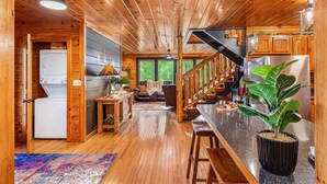 Interior de una cabaña de madera con cocina, sala de estar y una escalera.
