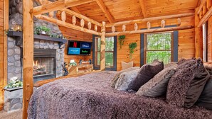 Un dormitorio rústico tipo cabaña con chimenea de piedra, televisor y una cama grande con almohadas mullidas.