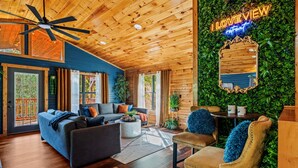 Een gezellige kamer met een houten plafond, een blauwe wand en een grote spiegel. Er is een bank, een stoel en een klein tafeltje met een plant.