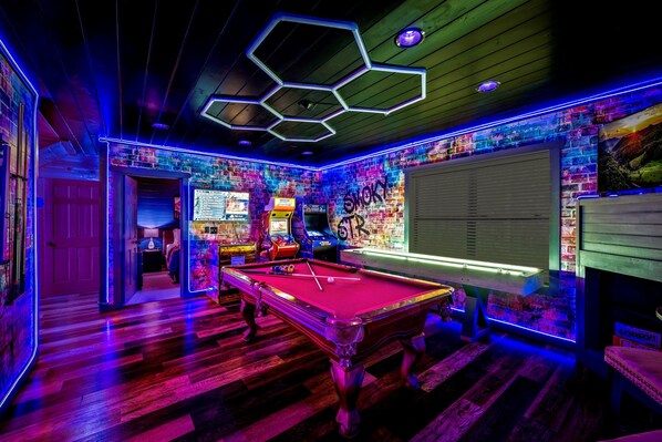 Uma mesa de bilhar em um ambiente com parede de tijolos e luzes neon.