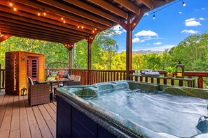 Uma banheira de hidromassagem em um deck de madeira, com uma cabana de madeira e móveis para área externa.