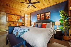 Quarto com painéis de madeira, cama, mesas de cabeceira, espelho e obras de arte nas paredes.