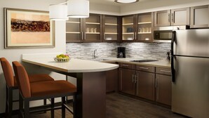 A modern kitchen with dark wood cabinets, a stainless steel refrigerator, a built-in oven, and a white countertop. - Comfortable Studio Suite in Rossford | Shared Indoor Pool + FREE Breakfast! (Rossford)