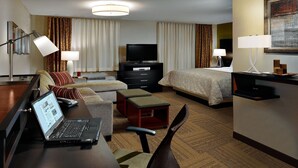 A hotel room with a bed, a desk with a laptop, a TV, and a seating area with a sofa and ottoman. - Comfortable Studio Suite in Rossford | Shared Indoor Pool + FREE Breakfast! (Rossford)
