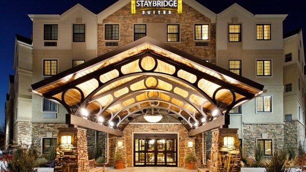Un hôtel Staybridge Suites doté d’une façade en pierre, d’une grande entrée et d’un patio couvert.