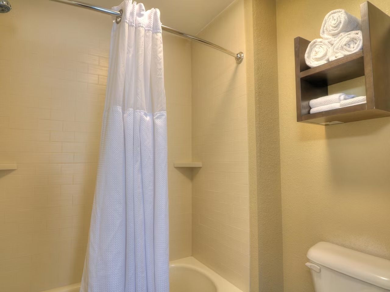 A bathroom with a shower curtain, a toilet, and a shelf with towels.