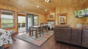 A wooden cabin interior with a dining area, sofa, and a television mounted on the wall.