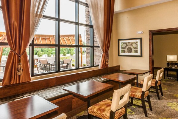 Ein Hotelzimmer mit einem großen Fenster, einer hölzernen Sitzbank und einem Essbereich mit Tischen und Stühlen.