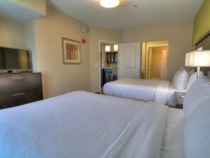 Ein Hotelzimmer mit zwei Betten, einem Schminktisch, einem Fernseher und einem durch eine offene Tür einsehbaren Badezimmer.