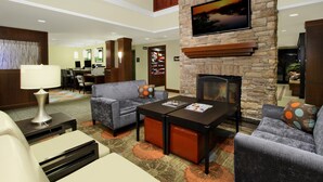 A hotel lobby with a fireplace, sofas, a coffee table, and a dining area.