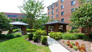 A landscaped courtyard with a gazebo, a brick building, and a pathway. - Comfortable Suite with Private Patio Near DC | Free Breakfast + On-Site Fitness Center (McLean)