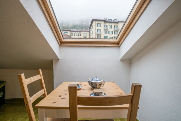 Una habitación pequeña con tragaluz, una mesa de madera con tetera y taza, y dos sillas de madera.