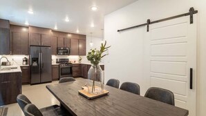 A modern kitchen with dark cabinets, a refrigerator, microwave, and a dining area with a wooden table and chairs. - Pool View | Bunk Beds | Fast Internet | Loft 32 (Saint George)