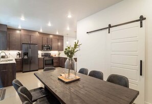 A modern kitchen with dark cabinets, a refrigerator, microwave, and a dining area with a wooden table and chairs. - Pool View | Bunk Beds | Fast Internet | Loft 32 (Saint George)