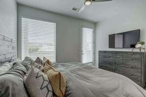 A bedroom with a bed, a dresser, a flat-screen TV, and a ceiling fan.