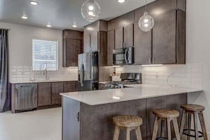 A modern kitchen with dark wood cabinets, stainless steel appliances, and a white island with stools. - Pool View | Bunk Beds | Fast Internet | Loft 32 (Saint George)