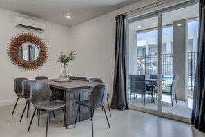 Un comedor moderno con una mesa redonda y sillas, un espejo decorativo y vista a una piscina a través de amplias puertas correderas.
