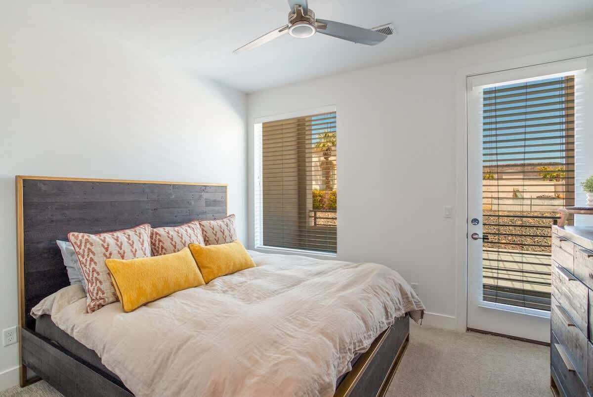A bedroom with a bed, a ceiling fan, a window with blinds, and a door.