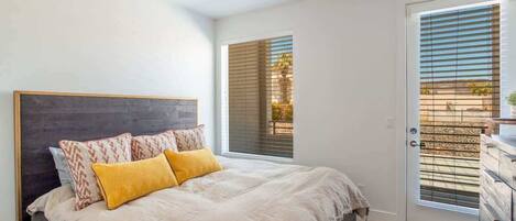 A bedroom with a bed, a ceiling fan, a window with blinds, and a door.