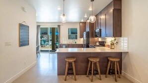 A modern kitchen with a central island, pendant lighting, and wooden stools. - Pool View | Bunk Beds | Fast Internet | Loft 32 (Saint George)