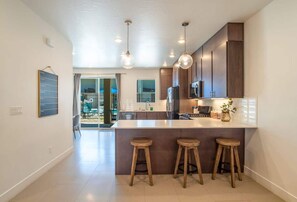 A modern kitchen with a central island, pendant lighting, and wooden stools. - Pool View | Bunk Beds | Fast Internet | Loft 32 (Saint George)