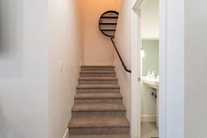 Una escalera alfombrada con barandilla y una lámpara fijada a la pared.