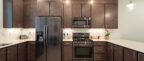 Una cocina moderna con armarios de madera oscura, electrodomésticos de acero inoxidable y encimera blanca.