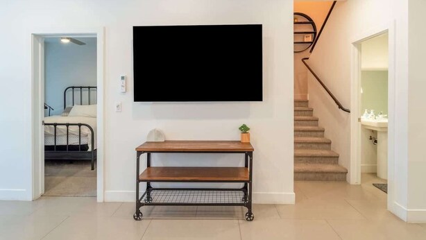 A modern living room with a mounted flat-screen TV, a wooden coffee table, and a staircase leading to a bathroom. - Pool View | Bunk Beds | Fast Internet | Loft 32 (Saint George)