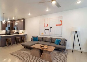A modern living room with a sofa, coffee table, and a kitchen area with bar stools. - Pool View | Bunk Beds | Fast Internet | Loft 32 (Saint George)