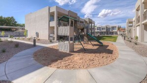 A playground with a slide and climbing structure, surrounded by a landscaped area with a concrete path. - Pool View | Bunk Beds | Fast Internet | Loft 32 (Saint George)