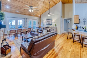 A spacious living room with a brown leather sofa, wooden flooring, and a ceiling fan.