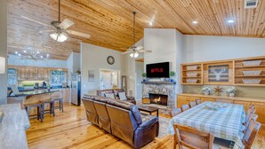 A spacious living room with a fireplace, leather sofa, dining table, and wooden ceiling.