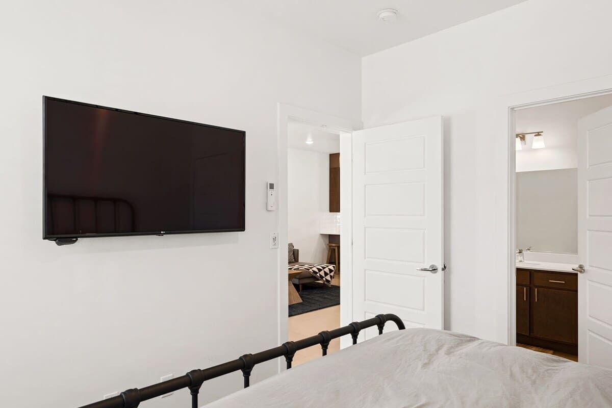 Quarto com uma cama, televisão fixada na parede e porta de acesso a um banheiro.