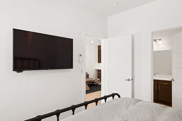 A bedroom with a bed, a TV mounted on the wall, and a door leading to a bathroom. - The Lofts #33 | Townhome Pool Resort | Poolside (Saint George)