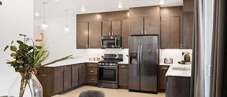 A modern kitchen with dark cabinetry, stainless steel appliances, and pendant lighting.