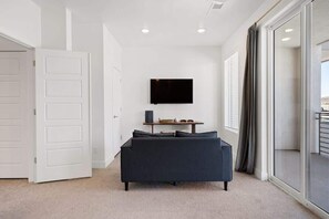 A modern room with a sofa, a flat-screen TV mounted on the wall, and a sliding glass door leading to a balcony. - The Lofts #33 | Townhome Pool Resort | Poolside (Saint George)