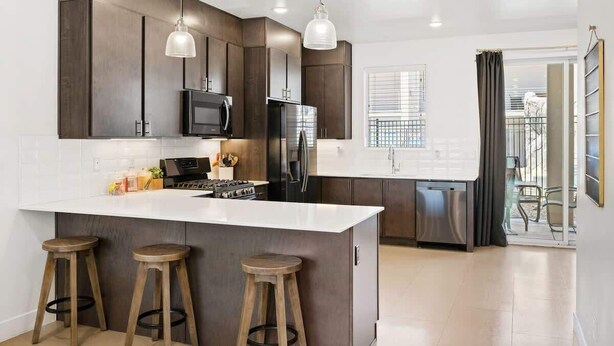 A modern kitchen with dark cabinetry, a white countertop, and three stools. - The Lofts #33 | Townhome Pool Resort | Poolside (Saint George)