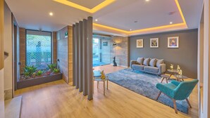 Una sala de estar moderna con un sofá gris, sillones turquesa y una pequeña mesa de centro. Hay una puerta de vidrio que da a un balcón con plantas.