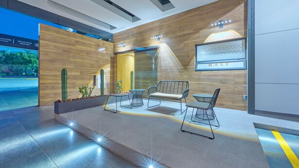 Un espacio interior moderno con una pared de madera, un cactus y una zona de estar con mesas y sillas.