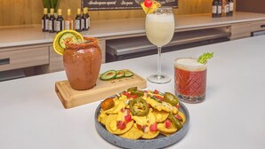Una zona de bar con un menú, una variedad de botellas y un plato de nachos con totopos y jalapeños.