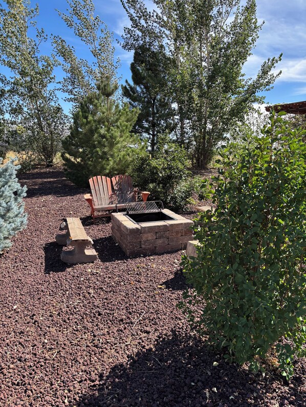 Un patio con un hogar de piedra, una silla Adirondack de madera y una parrilla de metal.
