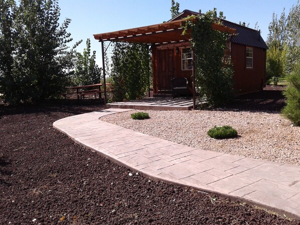 A wooden cabin with a pergola and a gravel pathway leading to it.