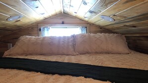 Una habitación con techo inclinado, un ventanal grande y una cama con cabecera oscura.