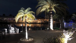 Ein Außenbereich bei Nacht mit Palmen, einem Pool und einer Anlegestelle.